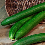 Three green cucumbers on a wooden surface with a woven basket in the background.