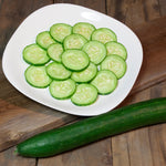 Sliced cucumbers on a white plate with a whole cucumber beside it on a wooden surface